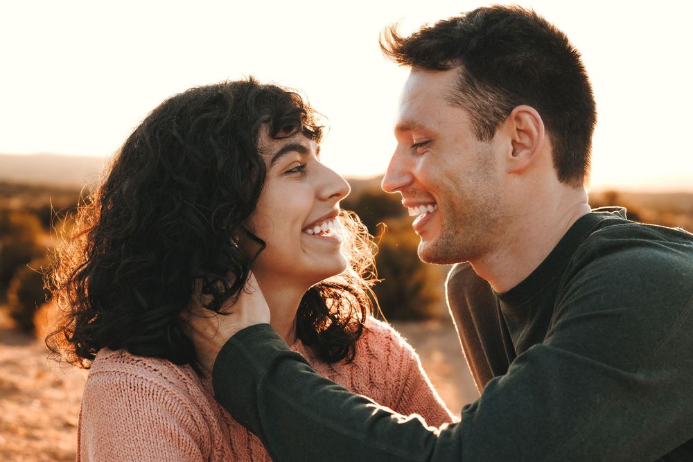 Smiling couple gazing at each other during golden hour, mans hand gently holding her face.