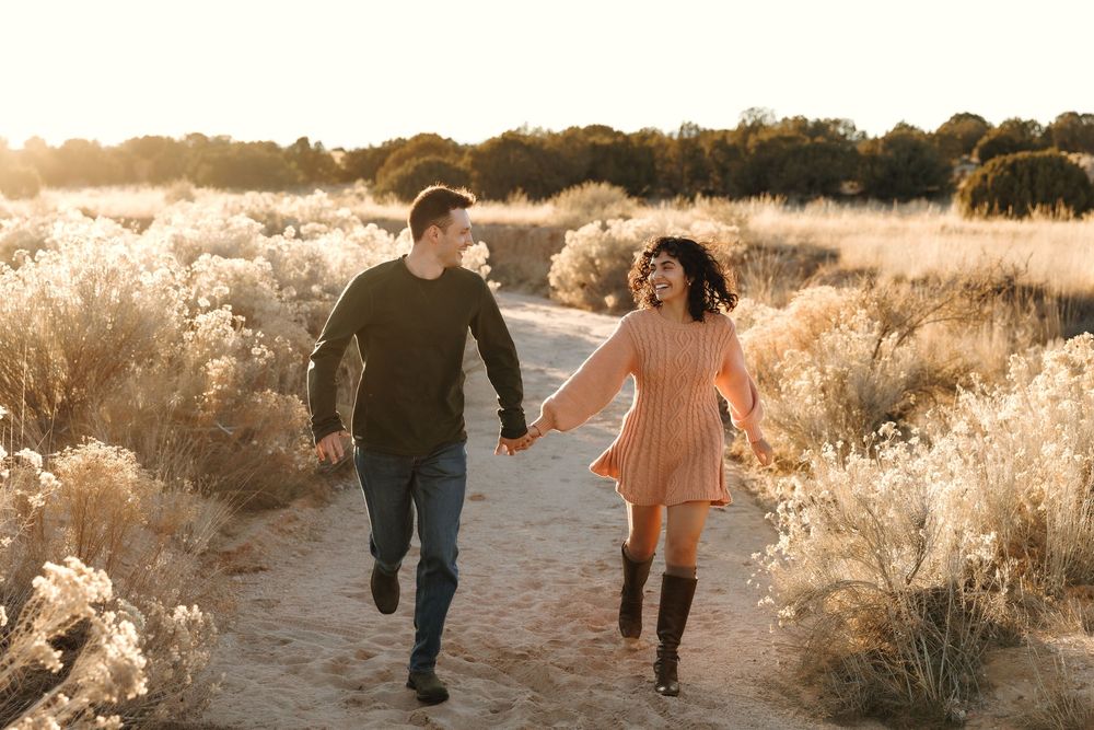Happy couple running hand in hand through sunlit desert trail at golden hour.