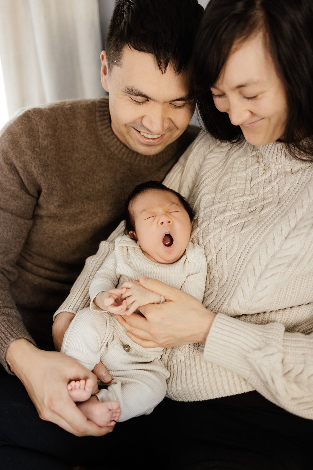 A newborn baby yawns while being held by his parents during his in-home photography session