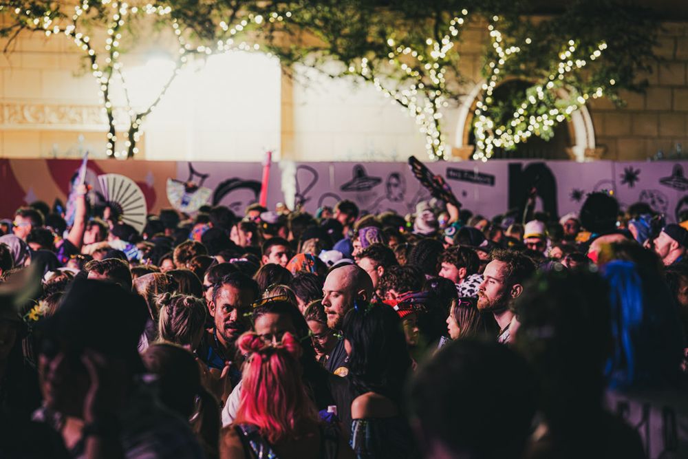 Wedding guests dance and celebrate on a crowded dance floor under twinkling string lights and decorations.