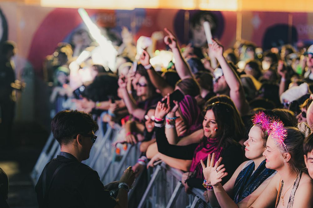 Energetic crowd at a concert raising their hands and dancing while enjoying live music performance.