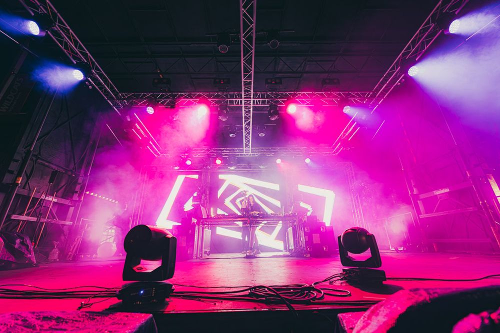Concert stage lighting setup with vibrant pink and purple hues illuminating a performance space.