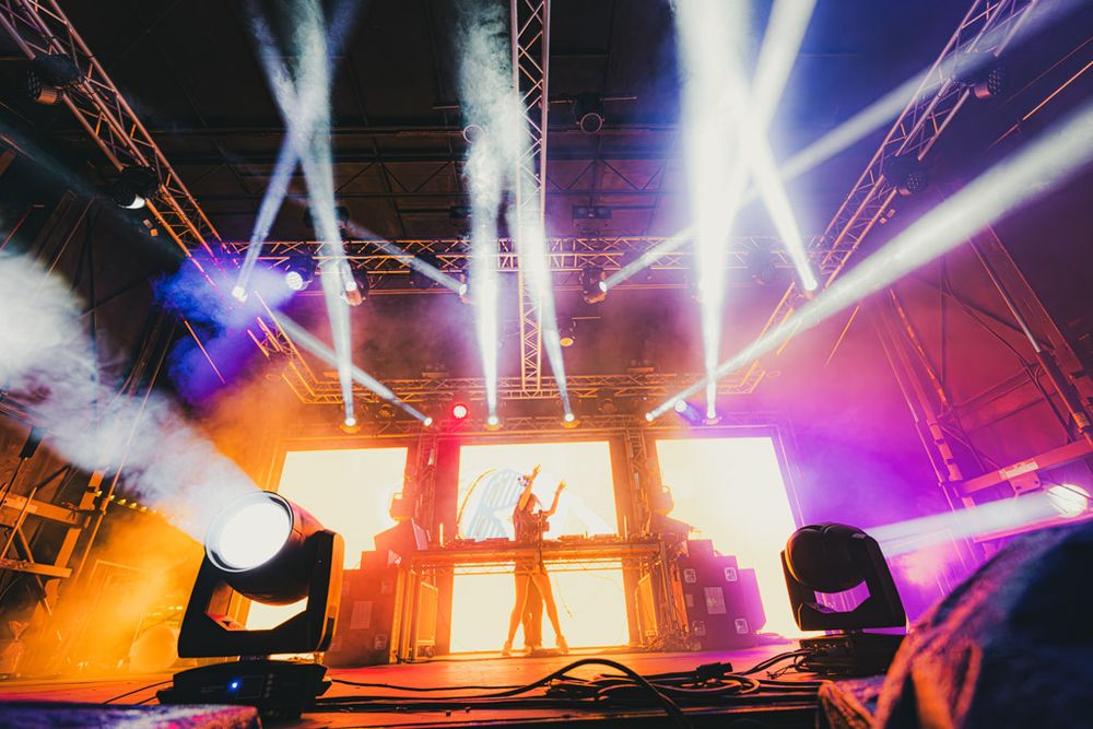 Concert stage illuminated with vibrant purple, pink and orange lighting effects during a live performance.