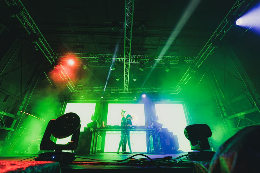 Concert stage illuminated with vibrant green and blue lights creating a dramatic atmosphere during a live performance.