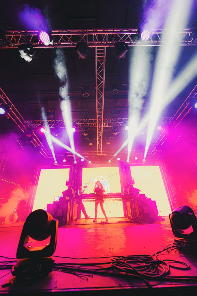 Silhouetted performer on illuminated stage with dramatic pink and purple lighting effects and smoke during concert performance.