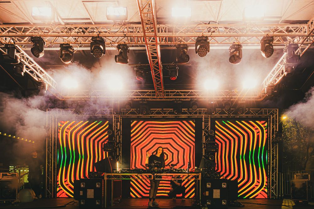 Concert stage with colorful geometric lighting patterns and silhouettes of performers creating a vibrant atmosphere.