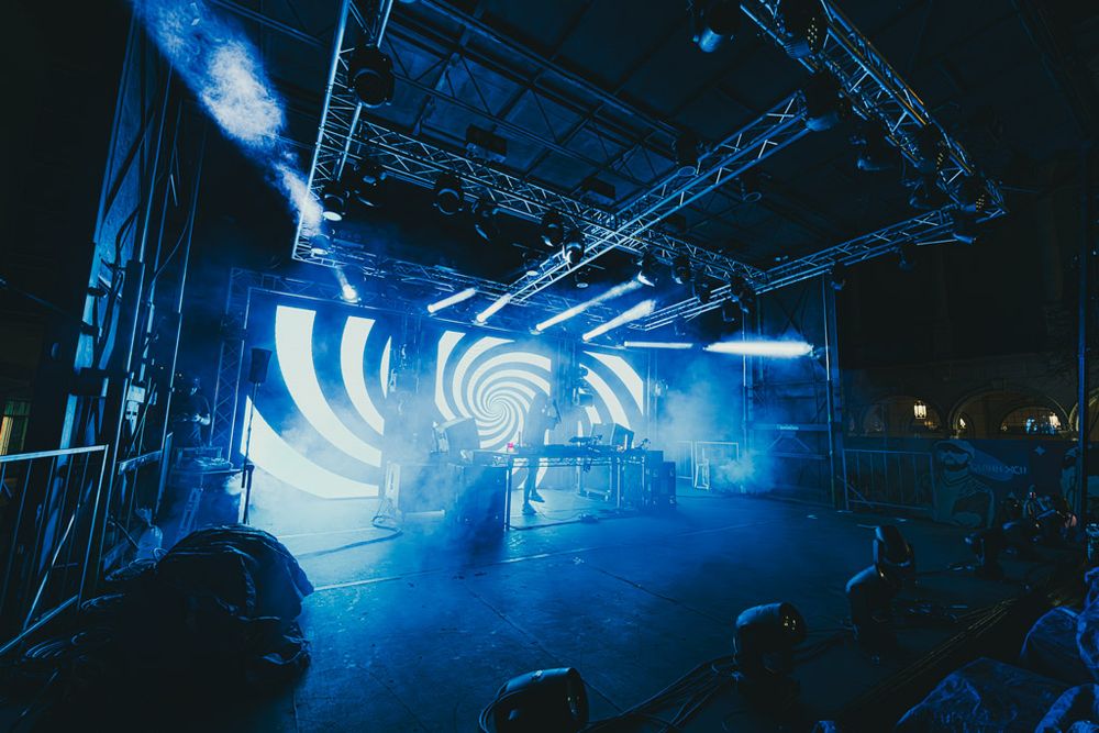 Concert stage lighting setup with blue atmospheric haze and silhouetted truss rigging creating dramatic theatrical effects.