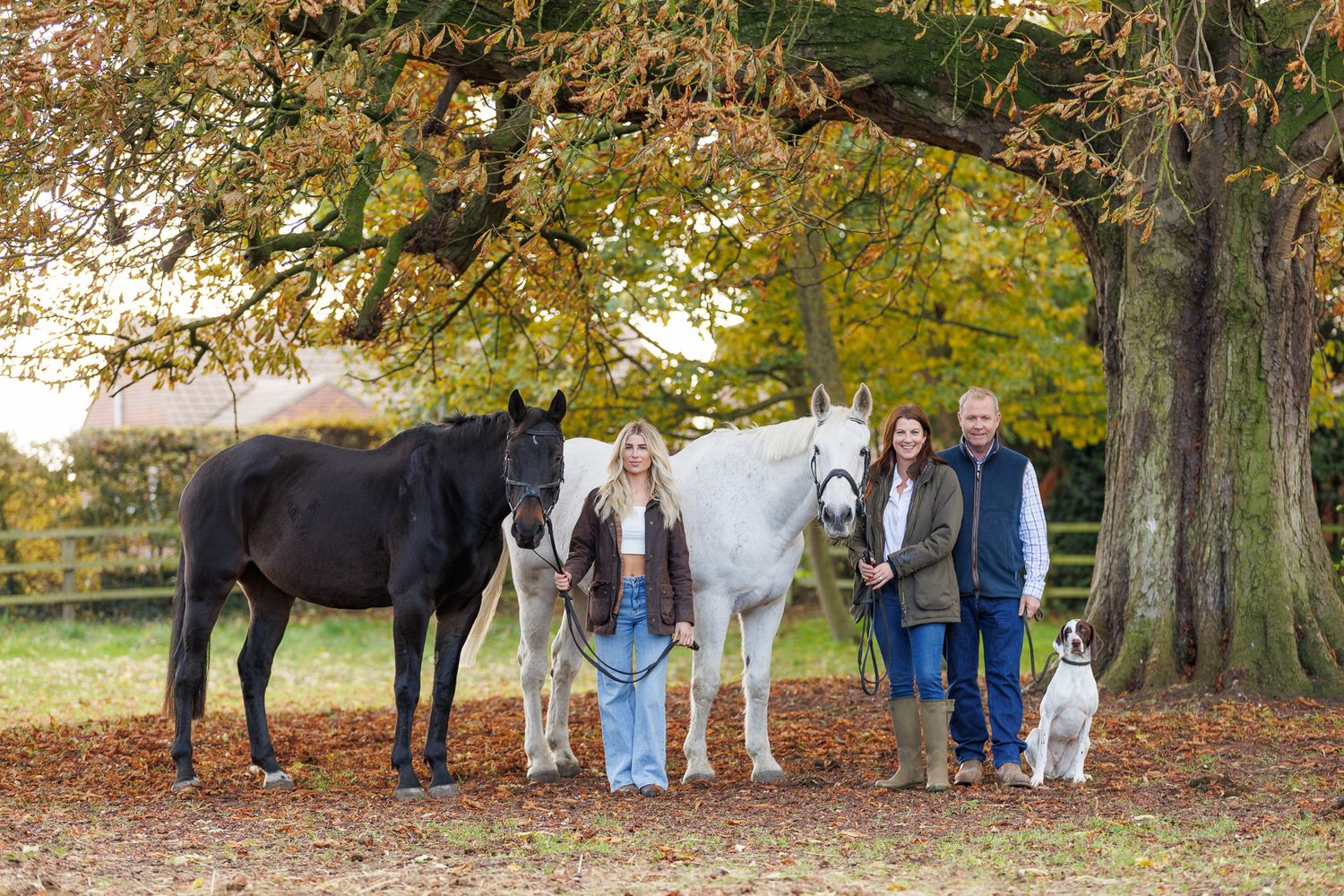 Two riders stand with their animals - a dog and a dark horse relaxing outdoors in a black and white photo.