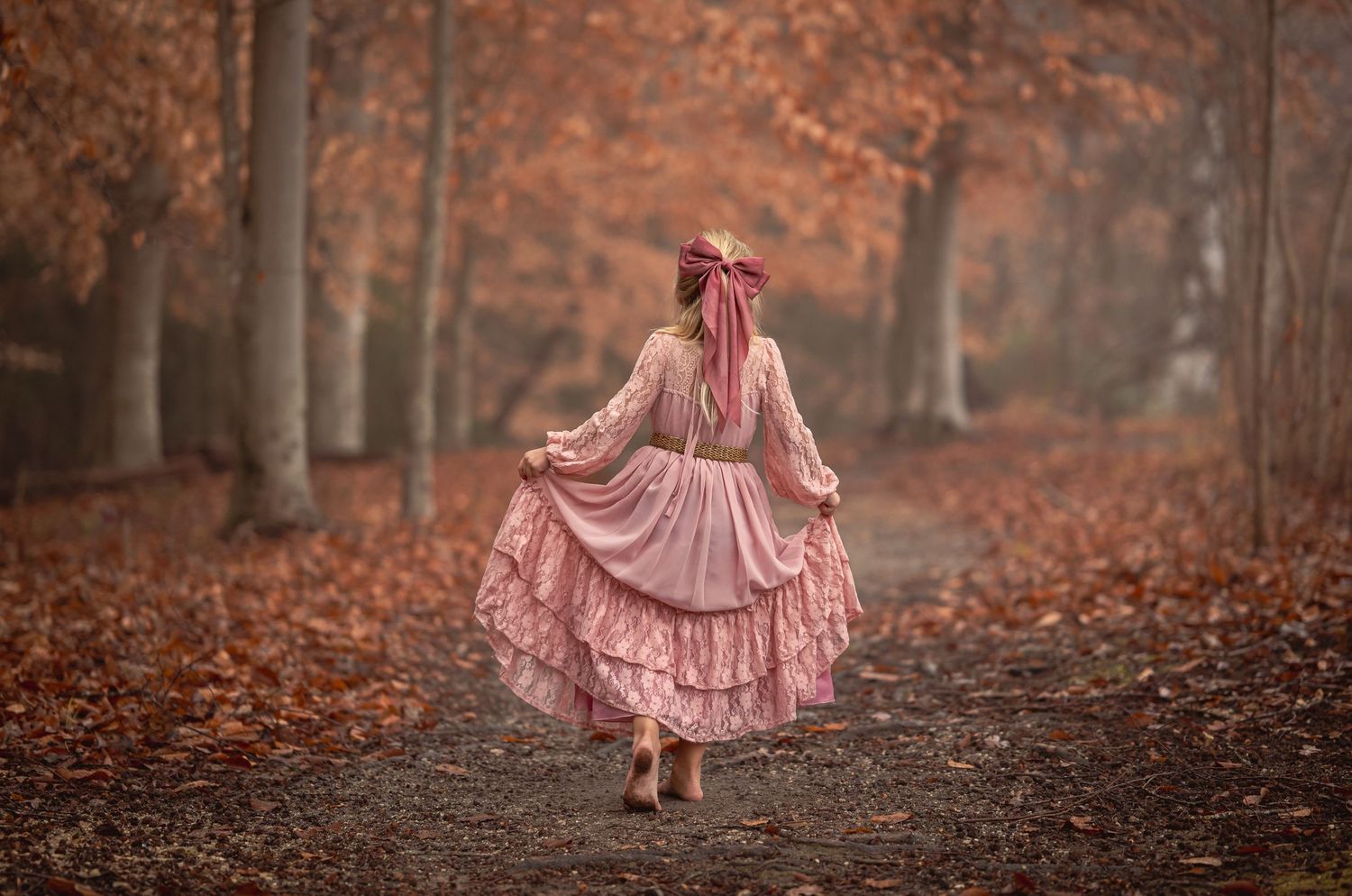 A pink dress flows gracefully through an autumn forest filled with fallen orange leaves and misty atmosphere.