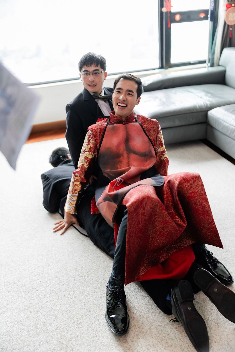 Groom in traditional Chinese red kua laughing with groomsmen on the floor.