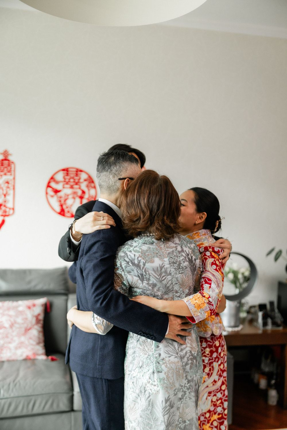Family sharing an emotional group hug during a Chinese wedding ceremony at home.