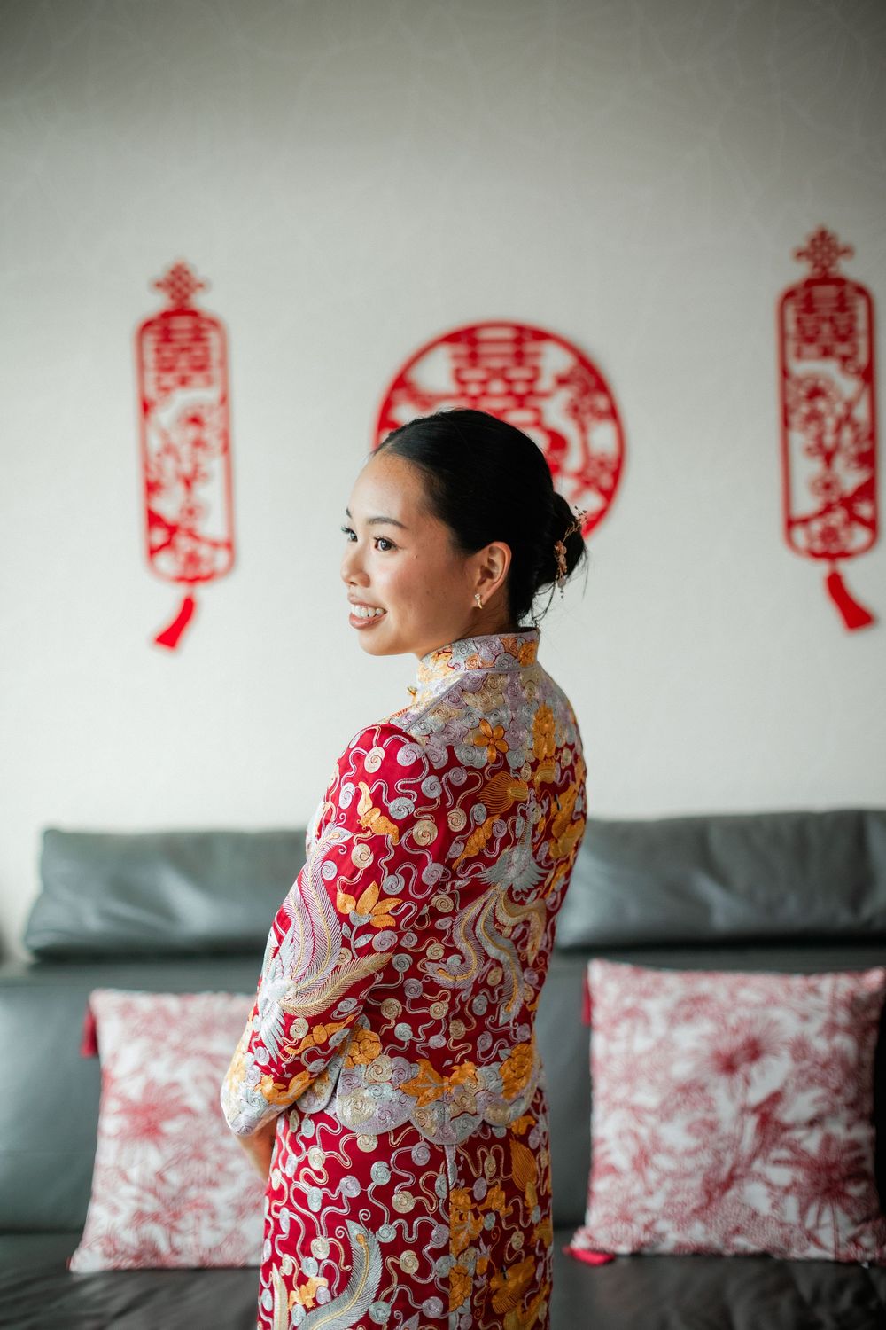 Bride wearing traditional red Chinese qipao gown posing in front of double happiness decorations.