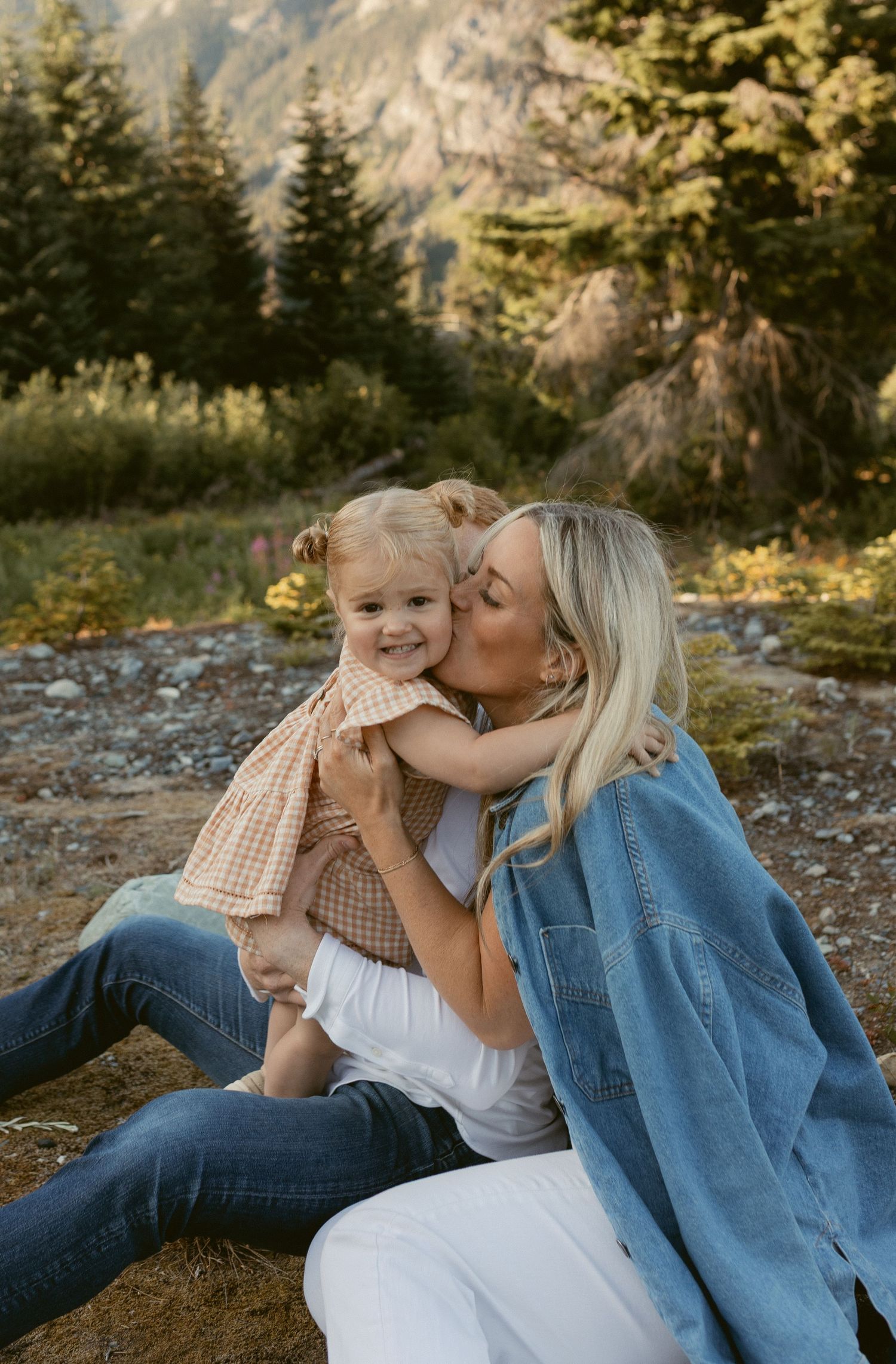 Mother and child share tender moments while lying on rocky mountain ground at sunset.