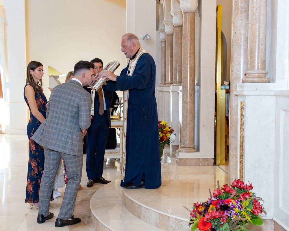 A baptism ceremony takes place inside an Orthodox church with religious icons visible on the walls at St. Demetrios Church in Weston, MA.