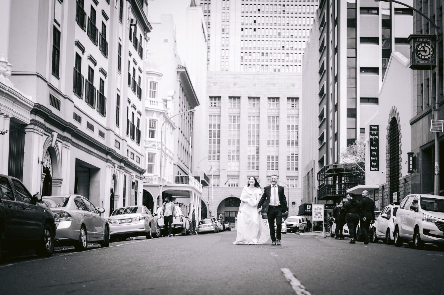 Black and white urban street scene with parked cars along tall buildings in a narrow city alley.