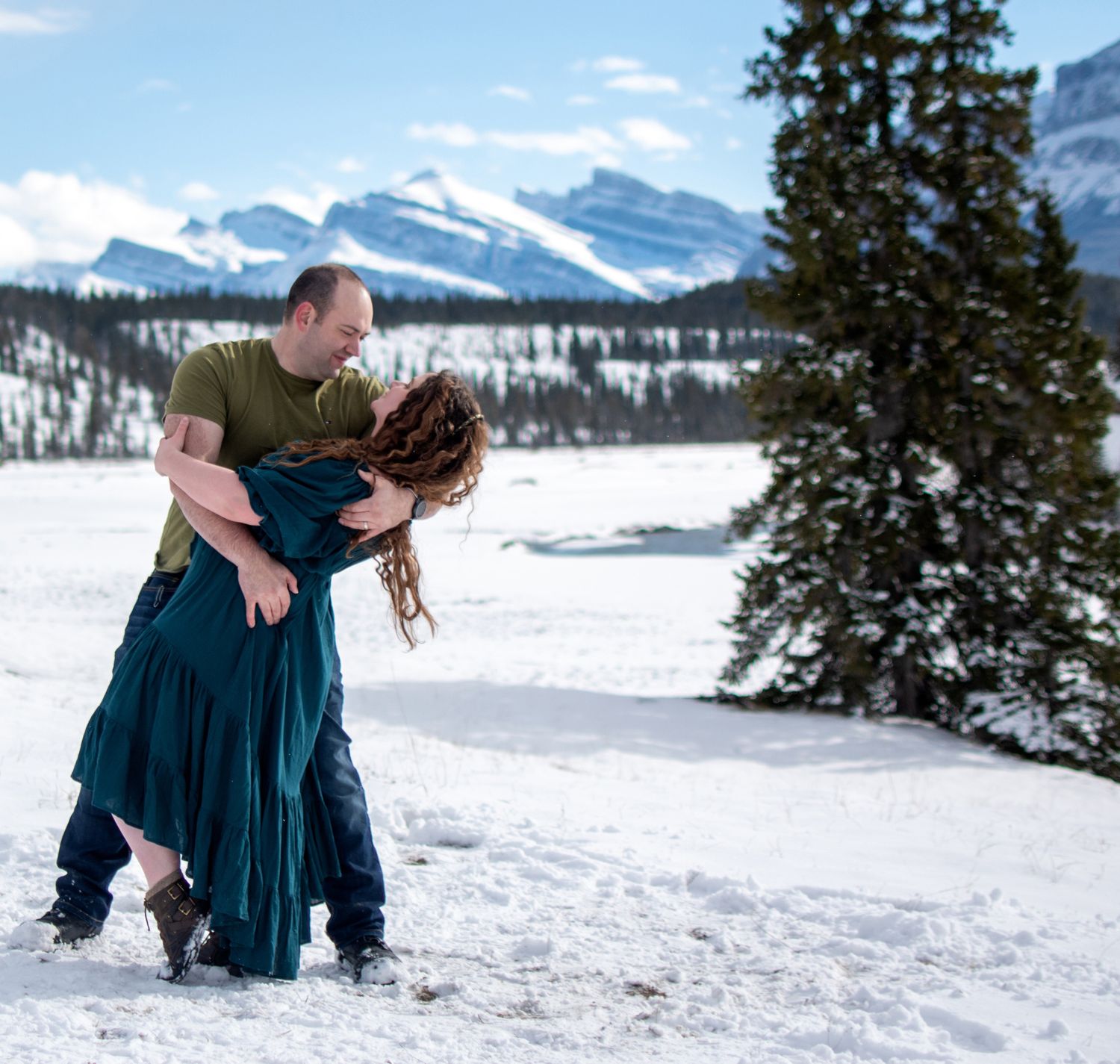 Couple playfully enjoying a snowy winter day in the mountains with snow-capped peaks in the background.