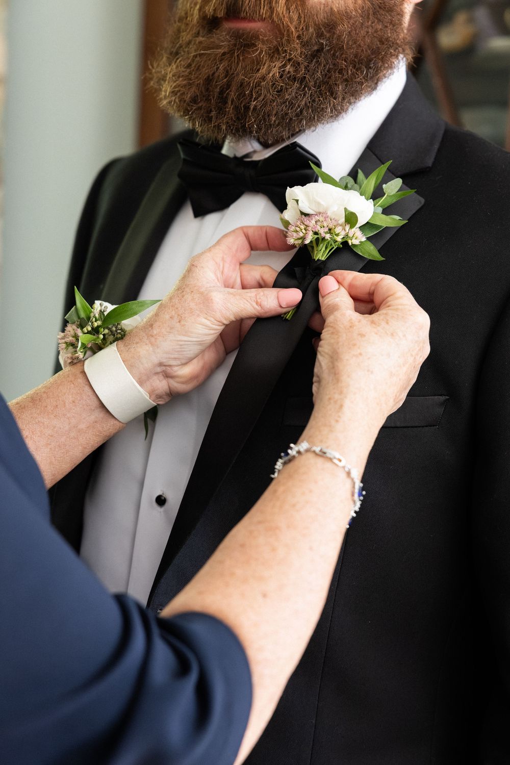 Close-up sequence of hands pinning a white boutonniere on a black tuxedo lapel.
