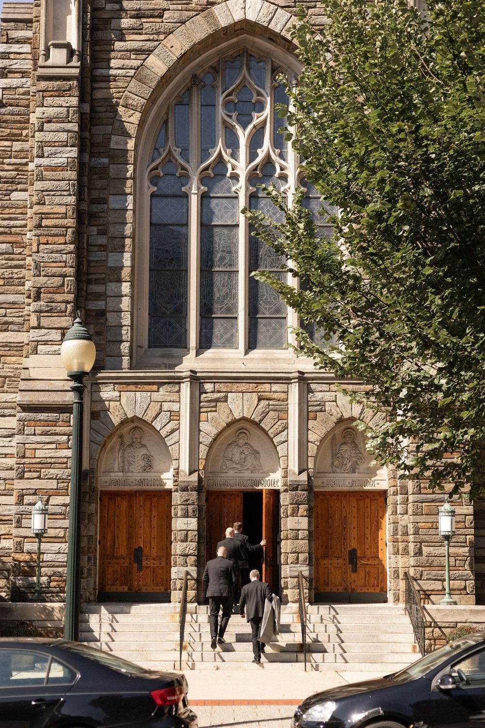 Gothic stone church entrance with arched windows and wooden doors on a sunny day.