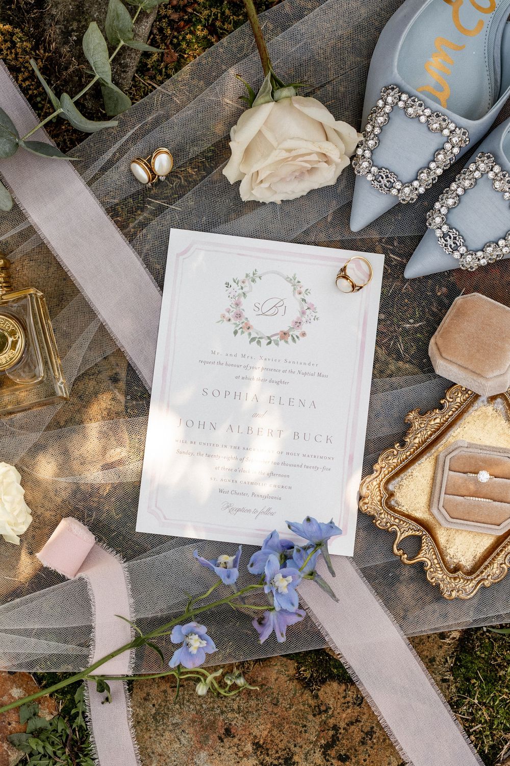 Wedding invitation suite with blue flowers, elegant typography, and delicate details laid out on stone.