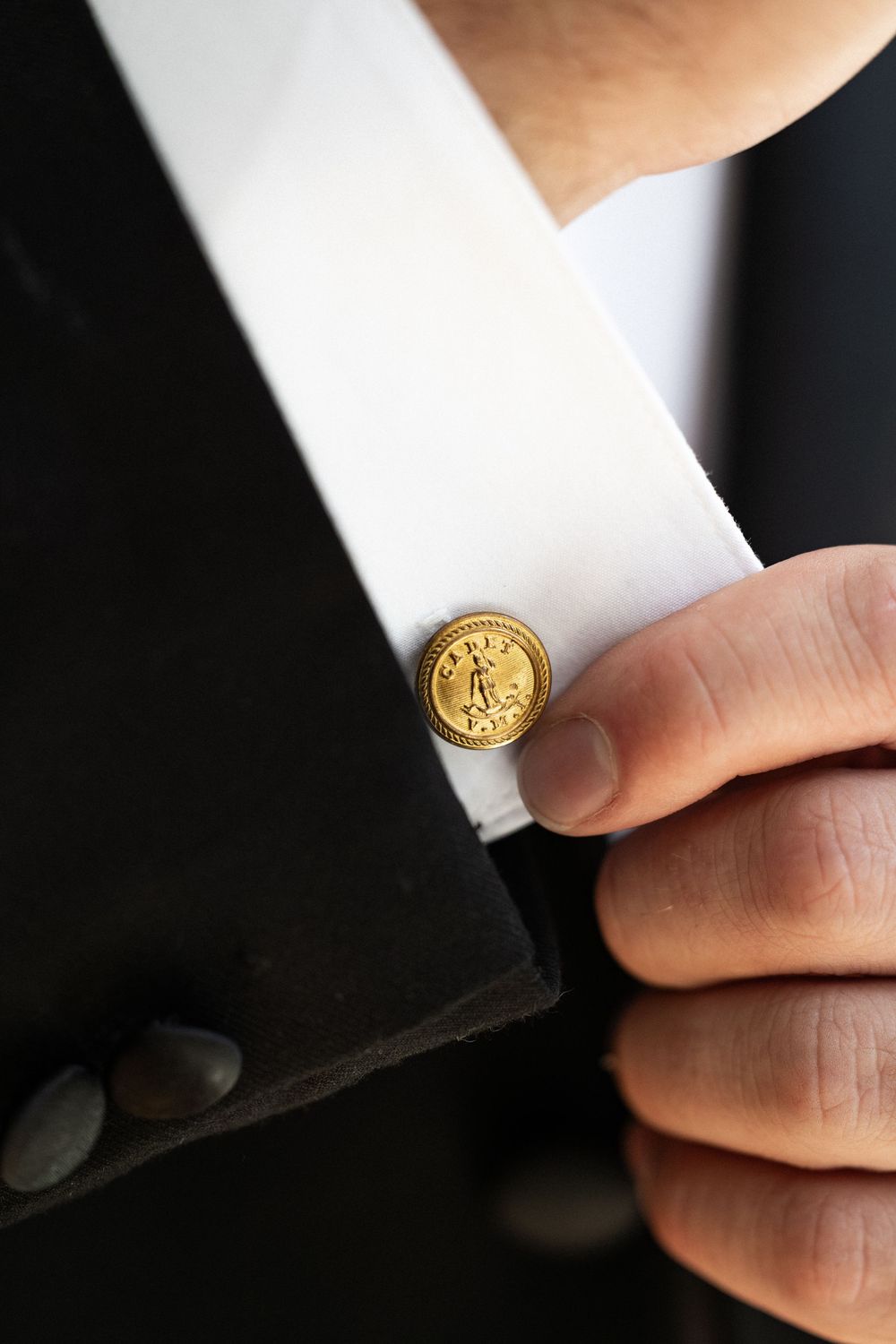 Close-up of a gold decorative button or cufflink on a white formal shirt collar.