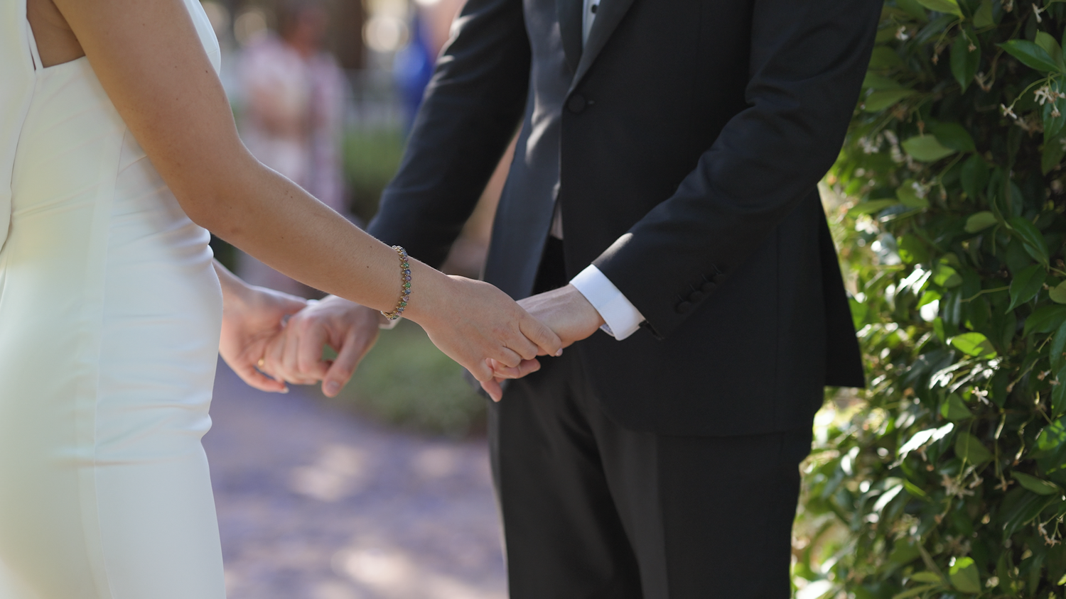 Couple walking hand in hand through a garden setting with natural foliage.