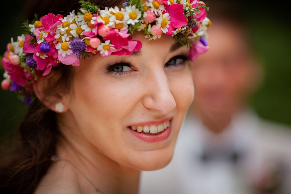 A colorful floral crown with pink and purple blooms adorns a head against a dark background.