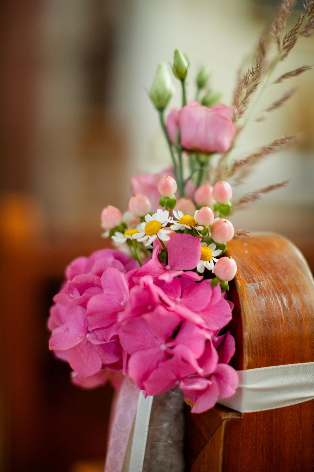 Pink floral pew decorations with hydrangeas and daisies adorn church seating.