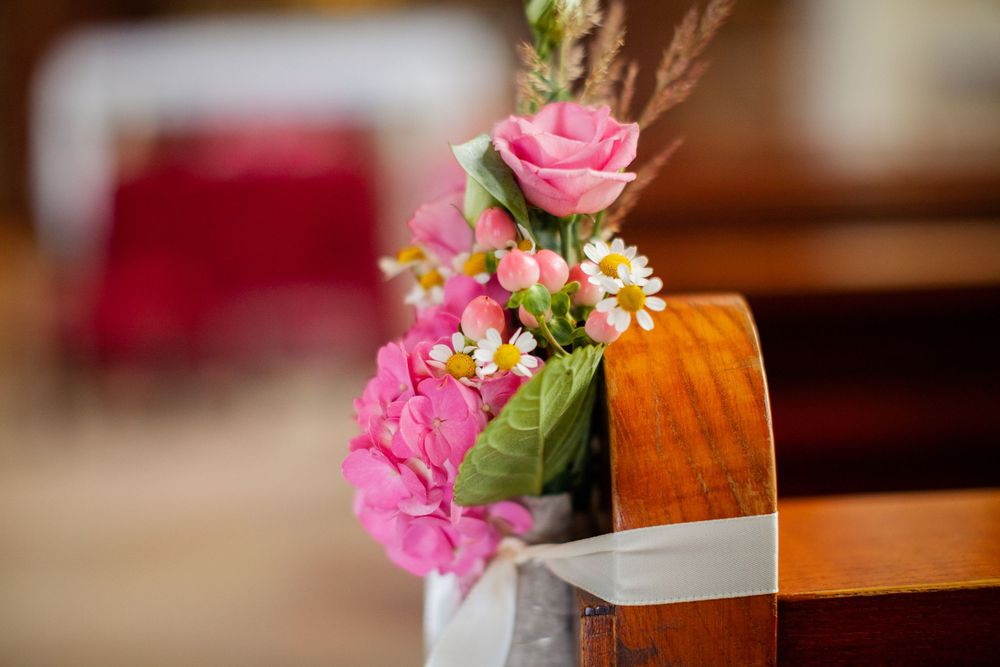 Pink roses and floral arrangements adorn wooden church pews.