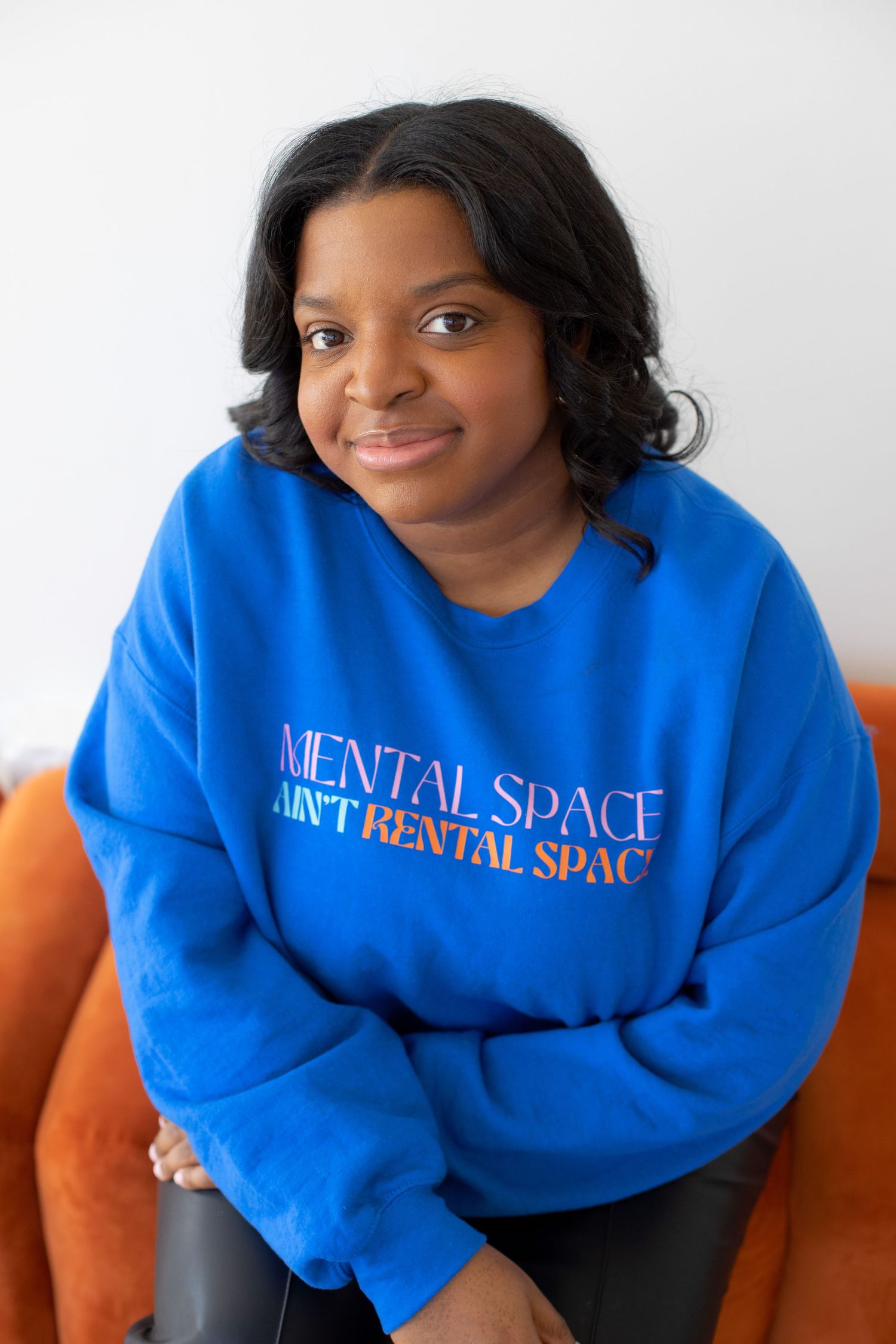Person wearing a bright blue sweatshirt with 'Mental Space' text sitting on an orange couch.