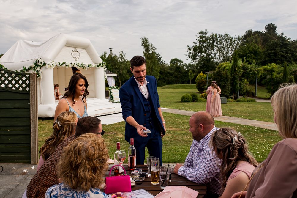 Wedding reception guests gathered at tables under white tent in garden setting.