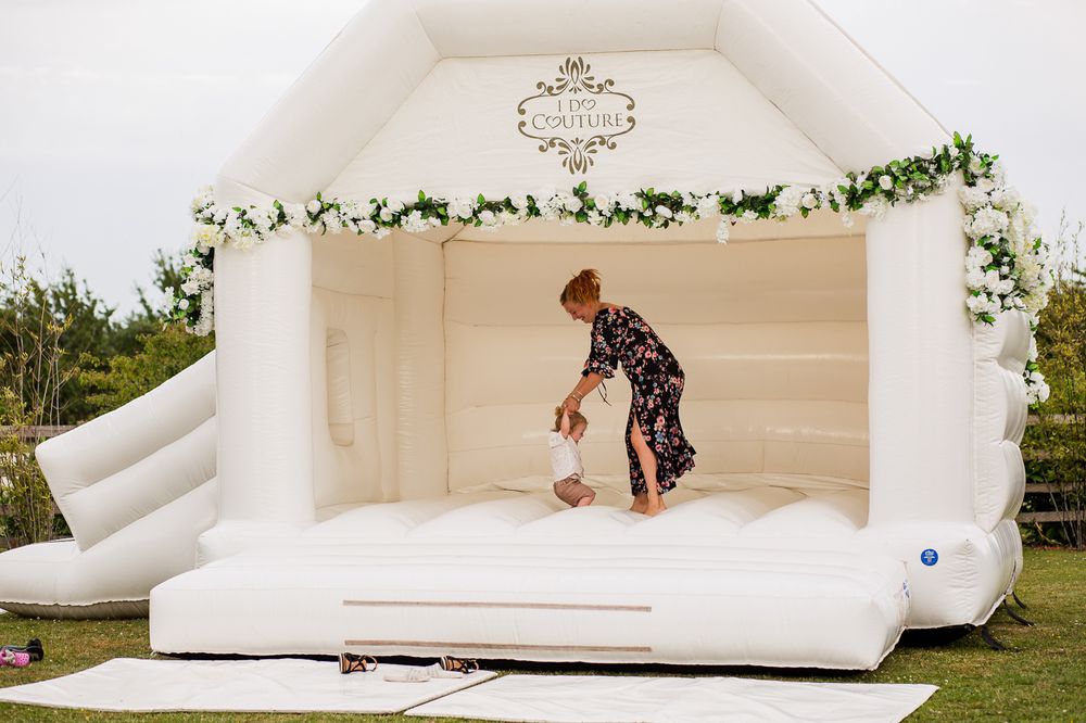 White inflatable bounce house decorated with greenery at outdoor wedding venue.