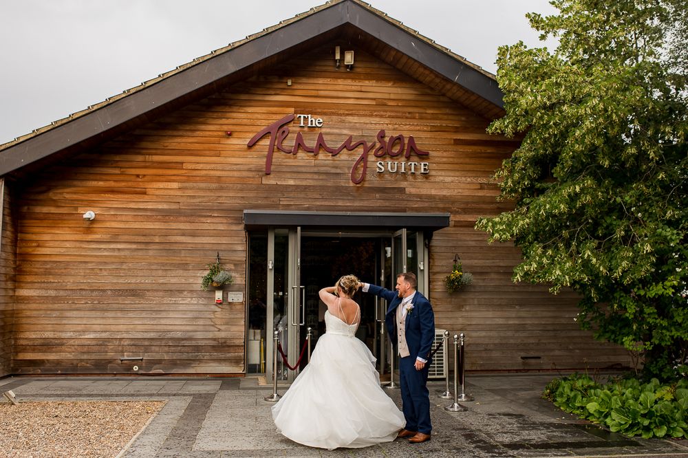 Playful wedding photo outside The Paragon Barn with rustic wood siding and signage.