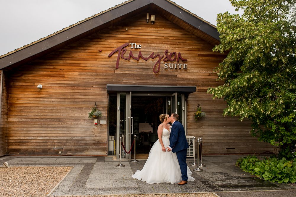 Couple poses outside rustic wooden venue The Paragon Barn during their wedding celebration.