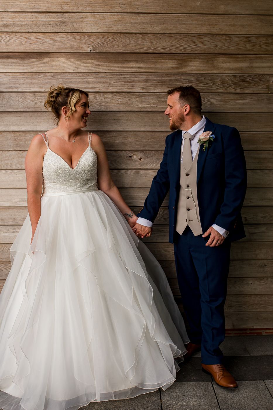 Elegant wedding portrait against rustic wooden wall showing formal attire and romantic connection.