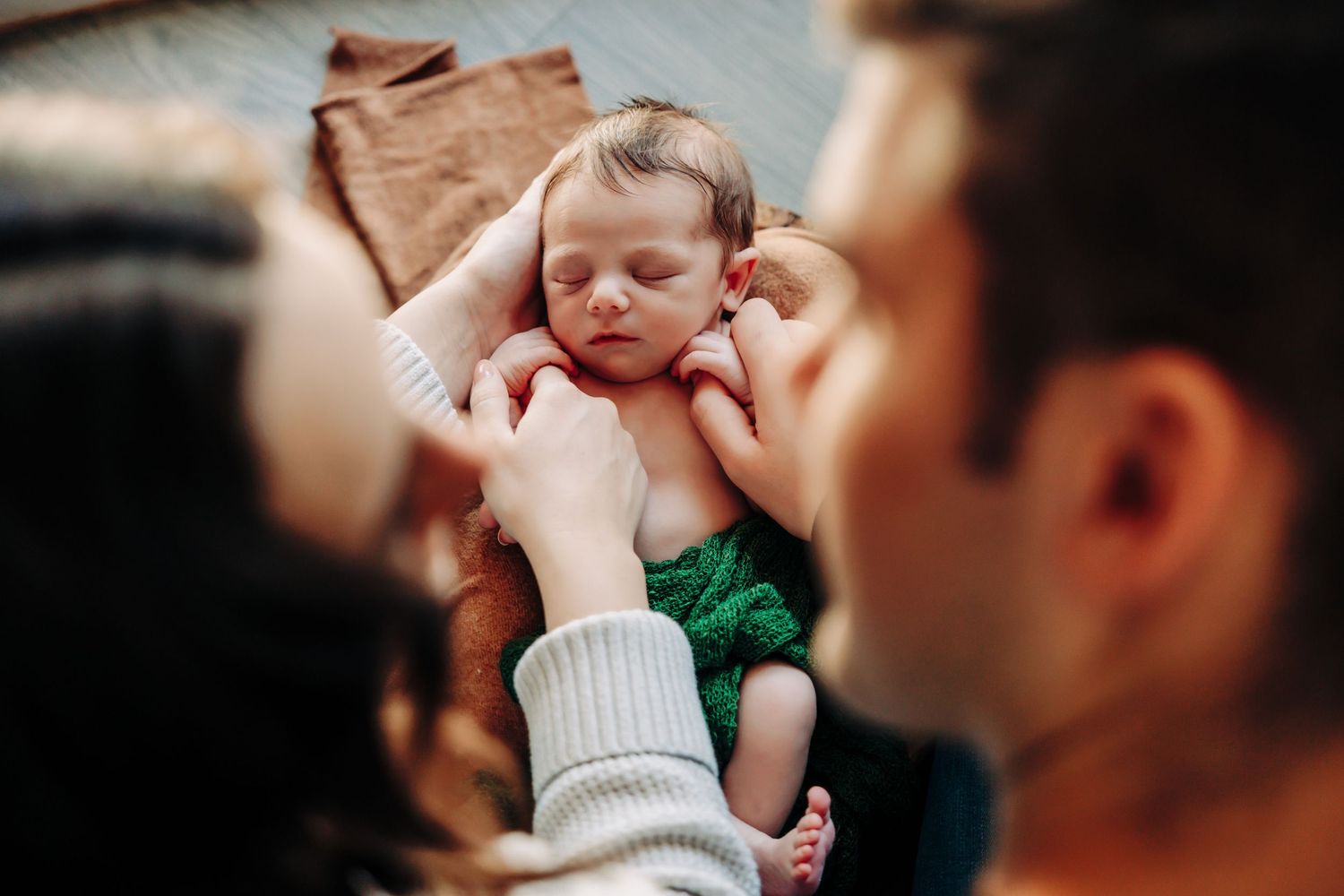 A newborn baby wearing a green wrap is gently cradled in someone's hands during a tender moment.