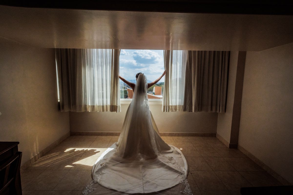 Panoramic view of a wedding dress in a sunlit room with dramatic window lighting.