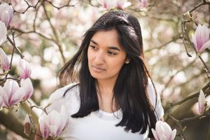 A person poses among blooming pink magnolia flowers in a spring garden setting.
