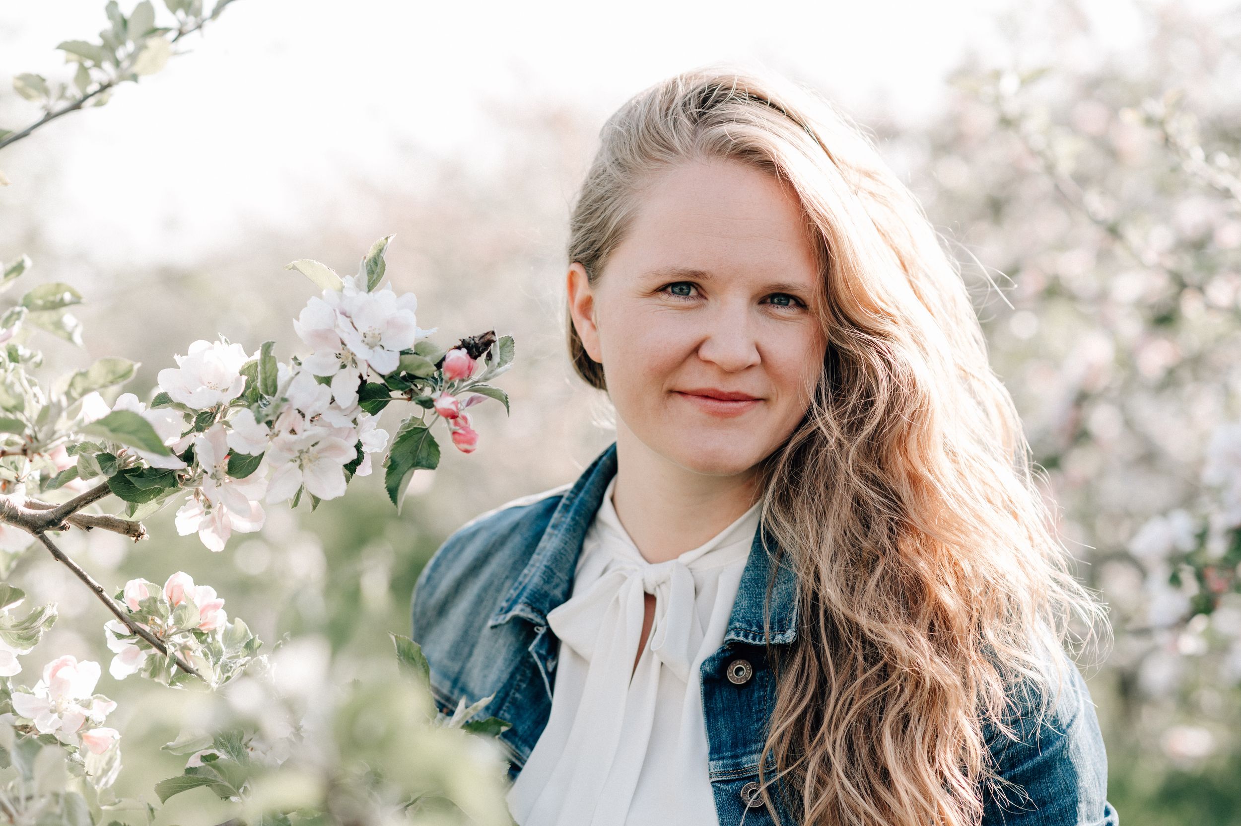 Spring portrait session in a blooming cherry blossom orchard with soft natural lighting and denim jacket styling.