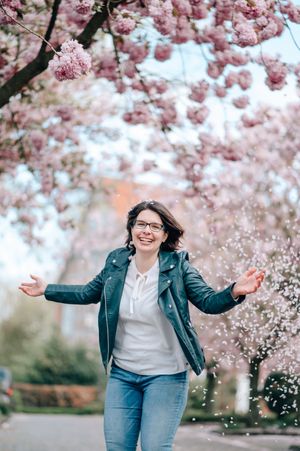 Joyful moment under blooming cherry blossoms with a green leather jacket and blue jeans on a spring day.