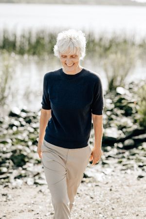 A person wearing a black t-shirt and beige pants walks outdoors in natural lighting.