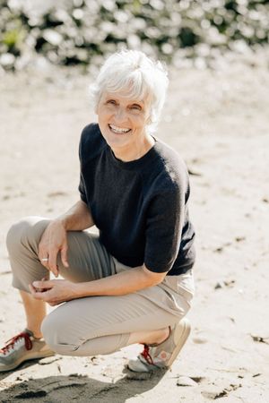 A person with white hair wearing a black shirt and khaki pants sits on a sandy beach in a candid photo series.