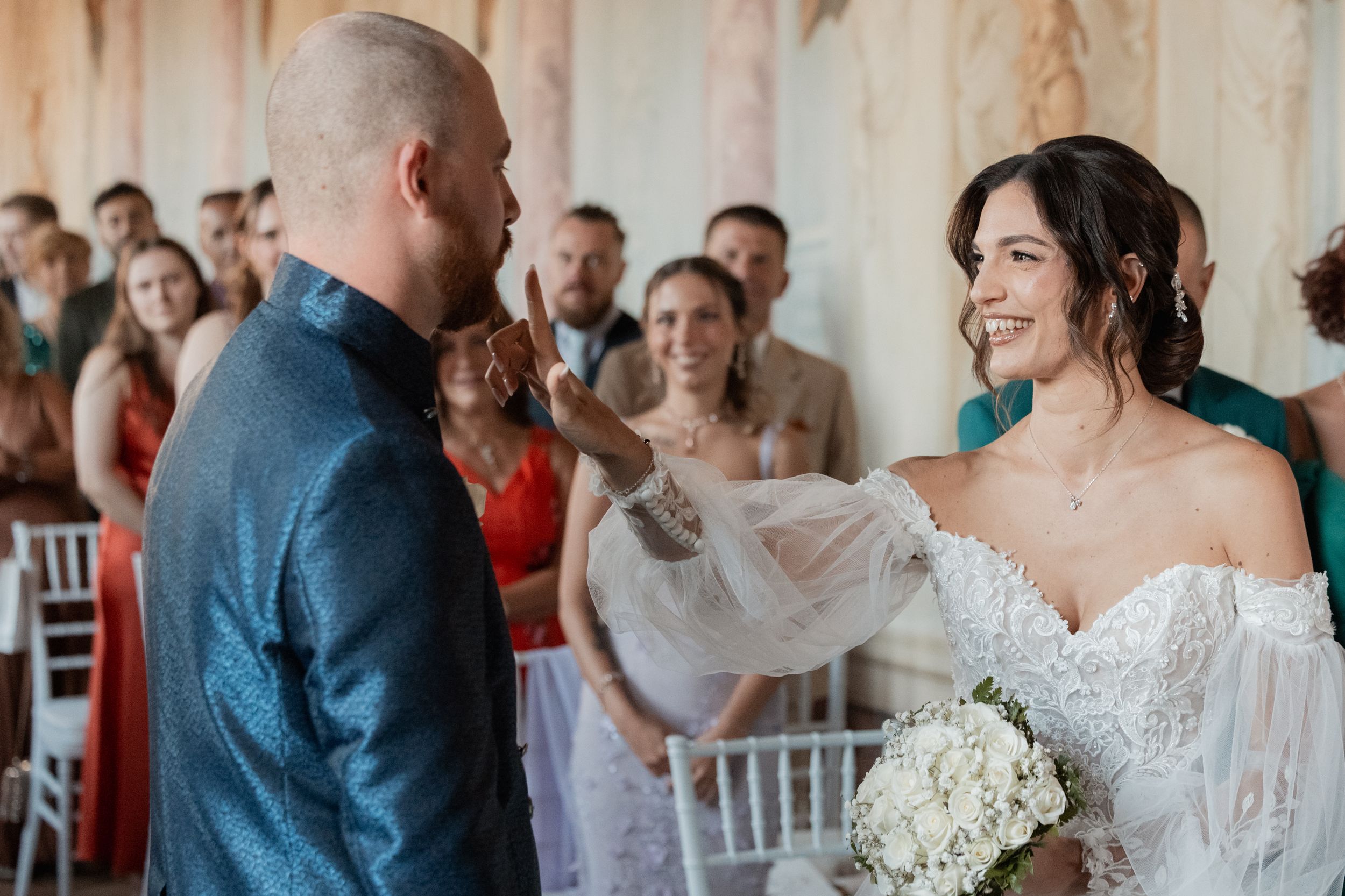 A joyful wedding ceremony moment with the bride in a white off-shoulder gown holding a white bouquet.