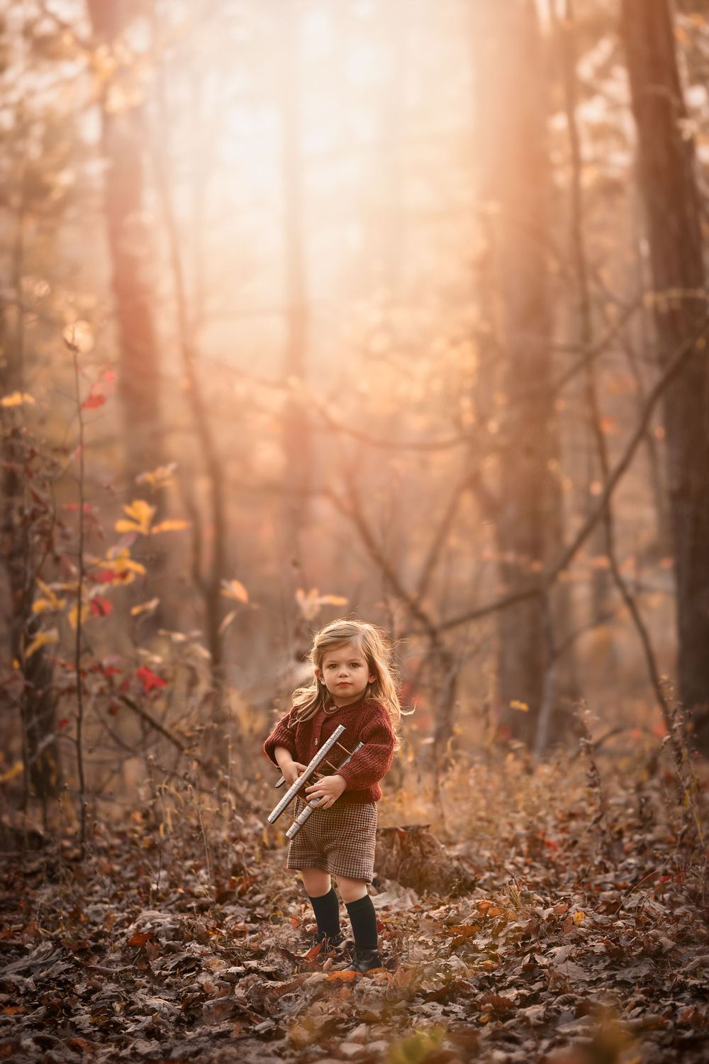 A child plays in a misty autumn forest with fallen leaves and sunlit trees creating a magical atmosphere.
