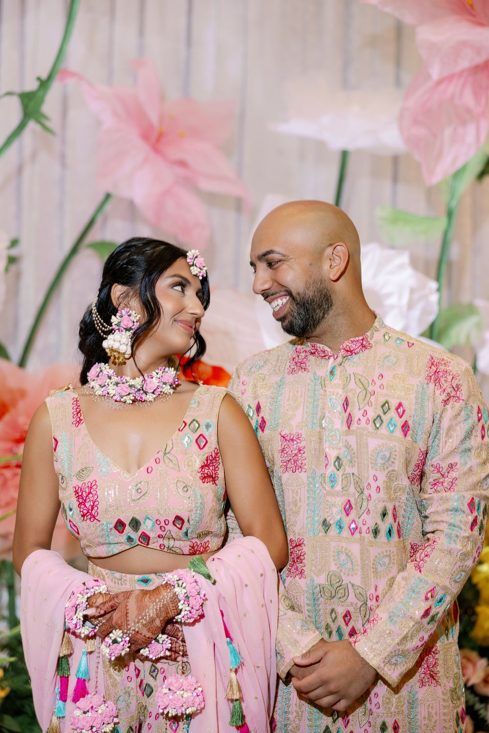 A couple in floral wedding attire embraces in a romantic sequence of photos with pink decor and cherry blossoms.