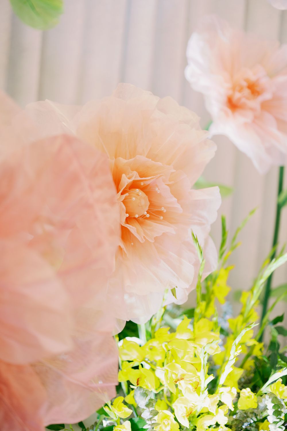 Delicate peach carnations arranged with bright yellow flowers and green foliage against a light background.