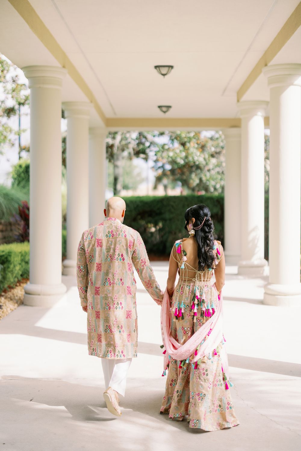 Figures in floral dresses walk through an elegant white columned portico on a sunny day.