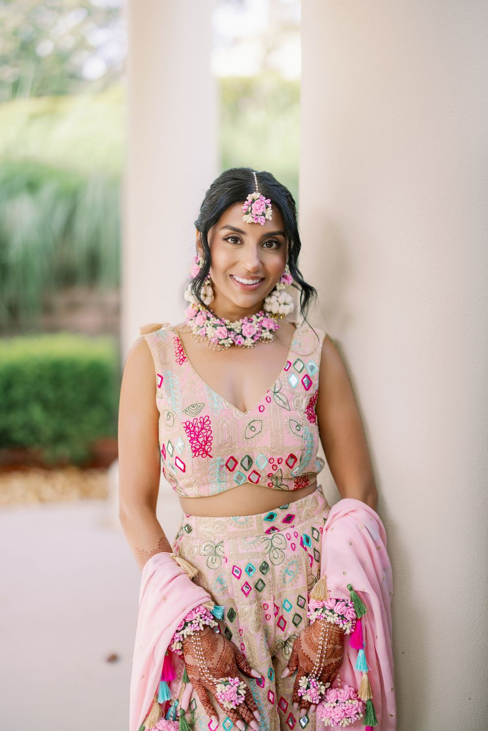 A series of photos showing someone wearing a floral embroidered lehenga in pink and beige tones at an outdoor venue.