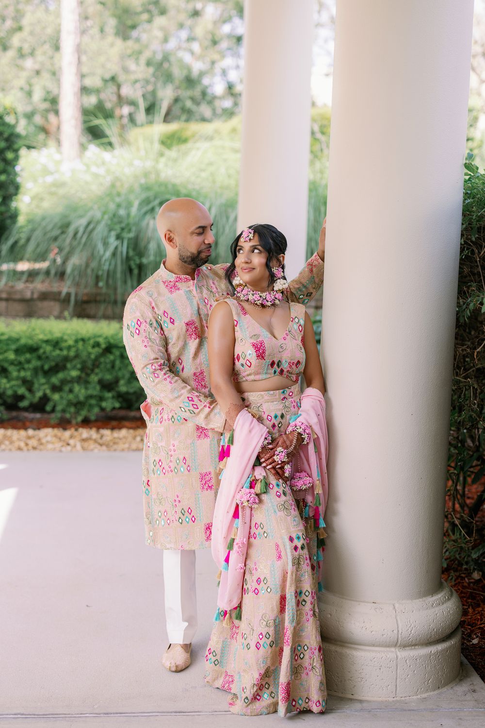 Romantic couple in matching floral outfits share intimate moments between white columns in an outdoor setting.