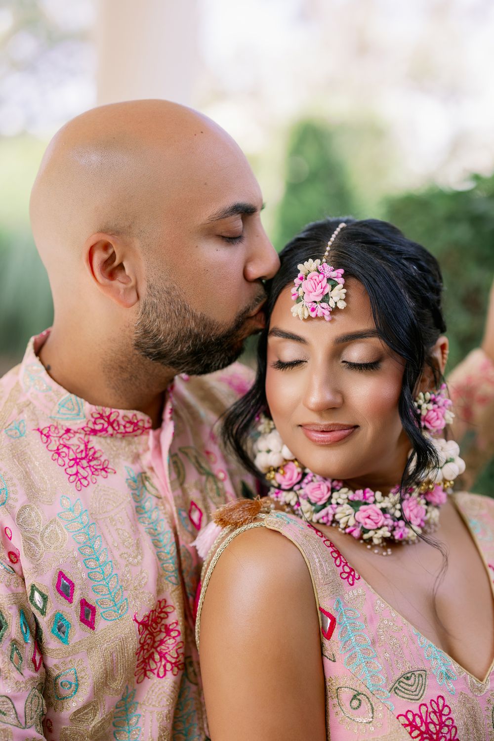 Romantic couple in pastel floral outfits share intimate moments in a garden setting with pink floral details.