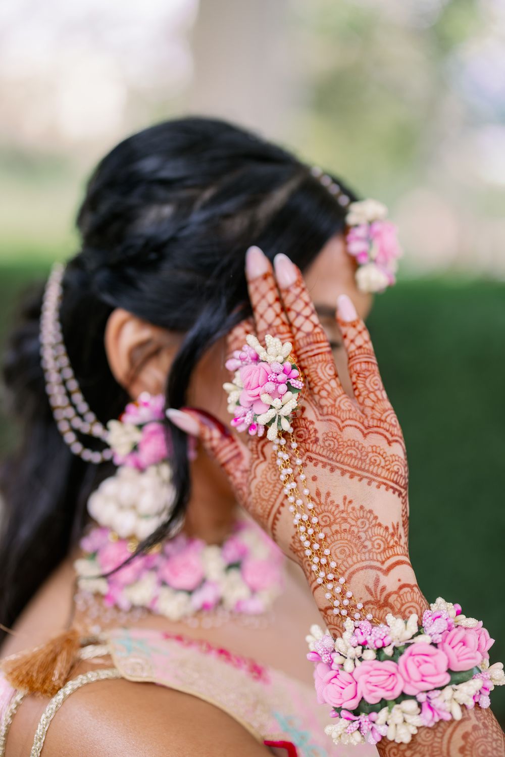 Intricate henna designs on hands adorned with pink flowers and jewelry create a beautiful bridal detail.